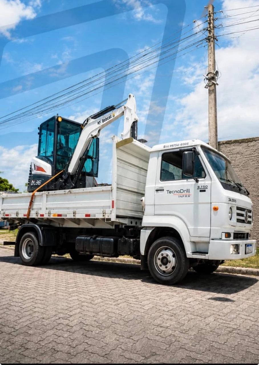 Caminhão branco transportando miniescavadeira Bobcat
